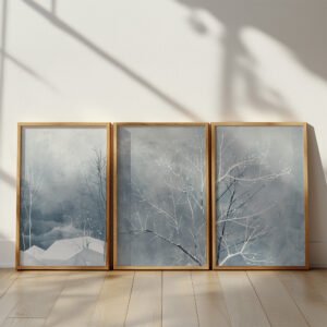 Three framed artworks of bare winter trees and abstract landscapes in soft gray-blue hues displayed on a light wooden floor with natural sunlight.