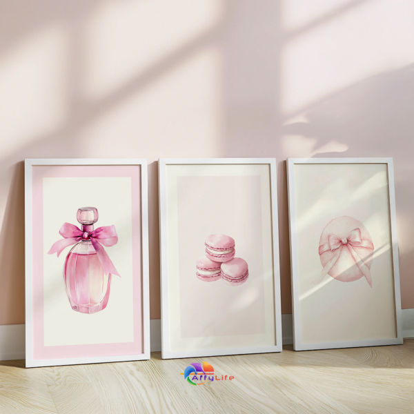 Pink Coquette Wall Art Set: Three white frames lean on the floor against a pink wall. The romantic prints of perfume, macarons, and powder puffs add a feminine and chic touch to the space.