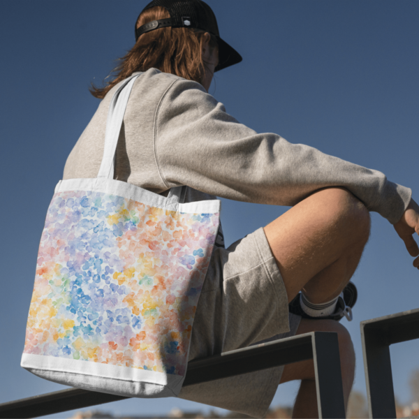 A man sitting on a railing with a floral-patterned canvas tote bag from the Spring Watercolor Seamless Patterns collection slung over his shoulder.