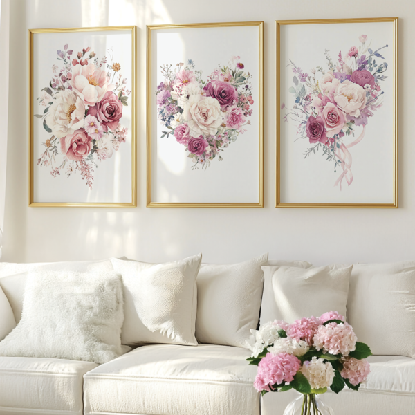 Three pastel floral posters in gold frames are displayed above a white sofa with white throw pillows. A vase of white and pink hydrangeas is on a coffee table.