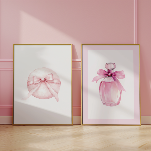 Pink Coquette Wall Art – 2 gold frames with powder puff and perfume prints leaning on a light floor against a pink wall. The artwork adds a soft, feminine, and chic touch.