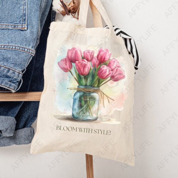 A beige canvas tote bag hanging on a chair featuring a tulip bouquet and the phrase "Bloom with Style" printed on the front. A chic use of the clipart designs.
