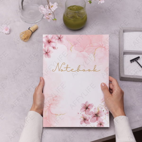 Hands holding a notebook with pink floral and gold design. Abstract flower clipart adds elegance.