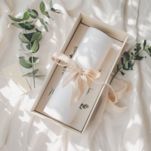 A printable poster rolled inside a shallow white gift box, tied with kraft ribbon, placed next to eucalyptus leaves and a blank gift card, photographed from above in soft natural light with a clean, minimal aesthetic