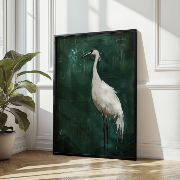 A framed Japanese Crane Art painting of a white crane with a red crown against a textured green background leans against a white wall near a potted plant.