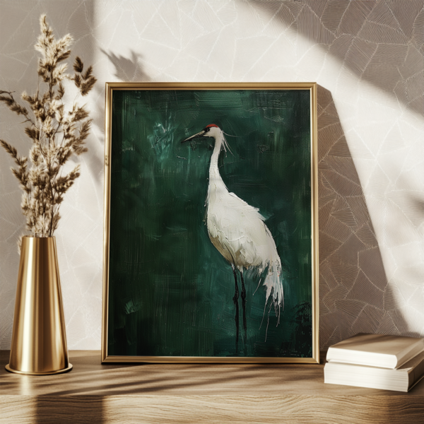 A framed Japanese Crane Art painting shows an elegant white crane on a rich green background. It is set on a wooden surface, with a gold vase of dried grass and stacked books nearby.