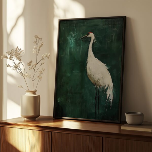 A framed Japanese Crane Art painting of a white crane with a red crown sits on a wooden cabinet. A vase with white flowers is nearby, illuminated by soft, warm light.