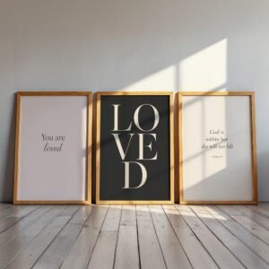 Christian Wall Art Set of three framed prints on a wooden floor in soft sunlight reading “You are loved,” “LOVED,” and a Psalm 46:5 quote, creating a warm and uplifting feel.